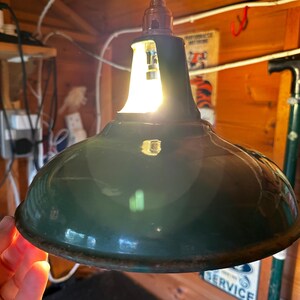 May include: A dark green, dome-shaped industrial pendant light fitting with a glossy enamel finish. The shade features a wide, curved rim with visible signs of rust along the bottom edge. A metal socket assembly sits at the top centre.