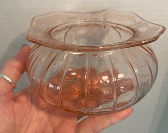 May include: A pink glass bowl with a scalloped rim and a ribbed design. The bowl has a delicate floral pattern etched into the glass.