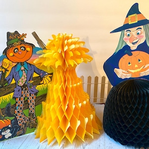 May include: A selection of vintage Halloween decorations. Features a scarecrow, a witch holding a jack-o'-lantern, a yellow honeycomb decoration, and a black honeycomb decoration. The scarecrow is orange and purple, and the witch is blue and green.