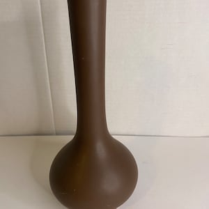 Peut inclure: Un vase en céramique brun avec une base ronde et bulbée et un long col fin.