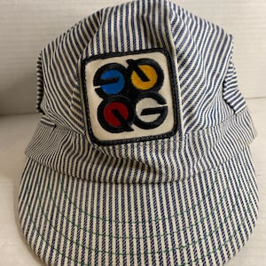 Könnte beinhalten: Eine blau-weiß gestreifte Arbeitsmütze mit einem quadratischen Aufnäher, der die Buchstaben "EOG" in einem farbenfrohen Design zeigt.