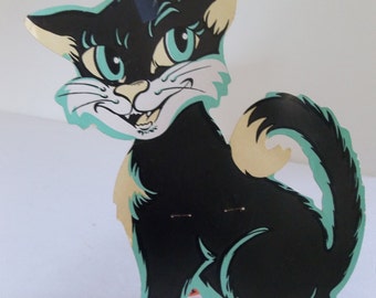 May include: A vintage black cat decoration with a cartoonish design. The cat has a smiling face with white teeth, light blue eyes, and light blue accents. The cat is sitting with its tail curled up.