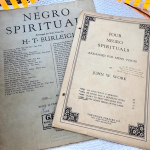 May include: Two vintage sheet music booklets with aged, off-white paper. The left booklet is titled Negro Spirituals by H.T. Burleigh. The right booklet is titled Four Negro Spirituals arranged for men's voices by John W. Work, published by Theodore Presser Co.
