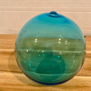 Op de afbeelding: Een witte keramische mok met een zwart handvat en de tekst "But first, coffee" in een handschriftstijl. De mok staat op een wit oppervlak. De mok is ongeveer 10 cm hoog.