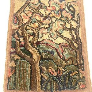 May include: Hand-hooked rug featuring a tree with colorful blossoms. The rug has a brown border and a detailed design with shades of brown, green, pink, and blue. The rug's texture is visible, showcasing the hand-crafted nature of the piece.