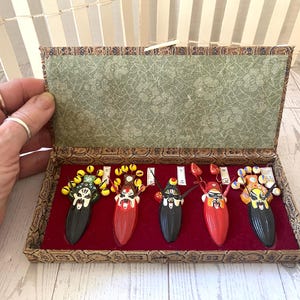 May include: A decorative box with five colorful, ornate Chinese opera masks. Each mask has a unique design with vibrant colors like red, yellow, and black. The masks are displayed on a red velvet surface within the box.
