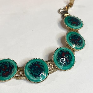 May include: A vintage gold-tone bracelet featuring six circular turquoise-colored enamel links with a dark red and navy blue pattern. The bracelet has a classic clasp closure and a delicate, scalloped edge design.