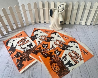 Könnte beinhalten: Halloween-Papiertüten mit orangefarbenen und weißen Designs, die Geister, Katzen und Hexen zeigen. Auf den Tüten steht "Trick or Treat". Eine weiße Geisterfigur und ein kleiner weißer Zaun sind ebenfalls im Bild zu sehen.