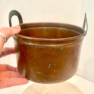 Caldero antiguo de cobre con patas, asas forjadas y relieve de hojas martilladas a mano.