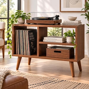Könnte beinhalten: Ein braunes Medienmöbel aus Holz mit vier konischen Beinen und einer Oberfläche, auf der ein Plattenspieler mit transparenter Abdeckung steht. Das Regal verfügt über offene Fächer mit Schallplatten, einer Holzkiste und gestapelten Büchern.