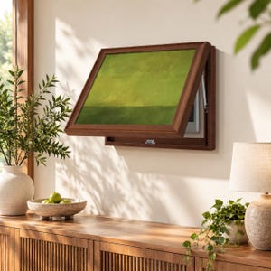 May include: A wall-mounted wooden display case with a hinged frame that opens outward. The frame features a dark brown finish and contains a rectangular panel with a two-tone green abstract design, revealing a hidden interior compartment.