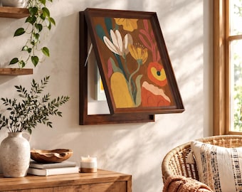 Puede incluir: Una vitrina de pared rectangular de madera con una puerta abatible que presenta una colorida pintura floral abstracta en tonos amarillo, naranja, rojo y verde azulado sobre un fondo marrón, revelando un espacio de almacenamiento interior blanco.