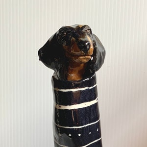 May include: A ceramic dachshund figurine with black and white stripes. The figurine is glazed and has a glossy finish.