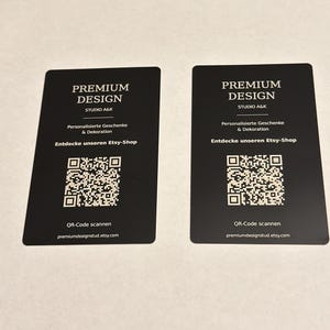 Könnte beinhalten: Zwei identische rechteckige schwarze Visitenkarten mit weißem Text und einem zentralen QR-Code. Der Text lautet PREMIUM DESIGN STUDIO A&K, Personalisierte Geschenke & Dekoration, Entdecke unseren Etsy-Shop, QR-Code scannen und premiumdesignstud.etsy.com.