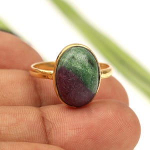 Può includere: Un anello in oro con una pietra preziosa cabochon di forma ovale caratterizzata da una netta divisione diagonale. La pietra presenta una sezione color magenta-viola intenso nella metà inferiore e una sezione verde testurizzata in alto.