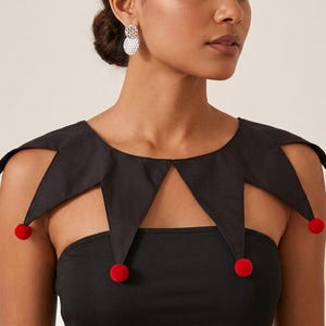 May include: A black detachable collar featuring a pointed, jester-style design with five distinct triangular flaps. Each point of the collar is finished with a small, round, bright red pom-pom. The collar is worn over a plain black strapless top.