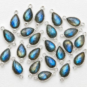 May include: A collection of teardrop-shaped labradorite charms, each featuring a faceted surface with iridescent blue and gray flashes, encased in a silver-toned metal frame with a small circular loop at both the top and bottom ends.