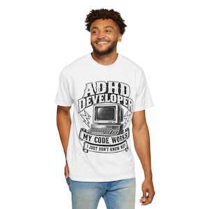 May include: A white short-sleeve t-shirt featuring a black graphic of a vintage computer with the text ADHD DEVELOPER, MY CODE WORKS, I JUST DON'T KNOW WHY. The design includes lightning bolt accents and a banner framing the computer illustration.