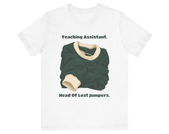 May include: A white short-sleeve t-shirt featuring a graphic of a dark green sweater with cream-colored ribbed cuffs and collar. The text "Teaching Assistant." is printed above the sweater, and "Head Of Lost Jumpers." is printed below.