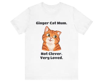 May include: A white short-sleeve t-shirt featuring a graphic of an orange tabby cat with a small tongue sticking out. The text above the cat reads Ginger Cat Mum. and the text below the cat reads Not Clever. Very Loved.