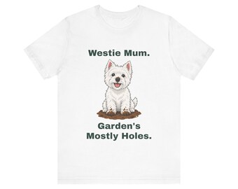 May include: A white short-sleeved t-shirt featuring a graphic of a West Highland White Terrier sitting in dirt with muddy paws. The text above the dog reads Westie Mum. and the text below the dog reads Garden's Mostly Holes.