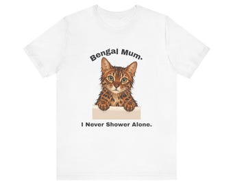 May include: A white short-sleeved t-shirt featuring a graphic of a brown spotted Bengal cat resting its paws on a ledge. Above the cat is the text Bengal Mum. and below the cat is the text I Never Shower Alone. in black font.