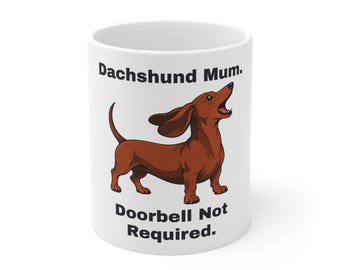 May include: A white ceramic mug featuring a brown dachshund illustration with its mouth open as if barking. The text above the dog reads "Dachshund Mum." and the text below the dog reads "Doorbell Not Required." in bold black lettering.