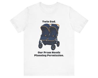 May include: A white short-sleeve t-shirt featuring a graphic of a navy blue double stroller with yellow accents. Above the stroller is the text Twin Dad. Below the stroller is the text Our Pram Needs Planning Permission.