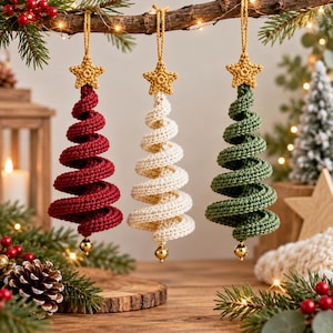 Könnte beinhalten: Drei spiralförmige Weihnachtsbaumschmuckstücke aus gehäkeltem Garn in Rot, Creme und Grün. Jedes Ornament hat oben einen kleinen gelben gehäkelten Stern und unten eine einzelne glänzende goldfarbene Perle, aufgehängt an einer dünnen Schnur.