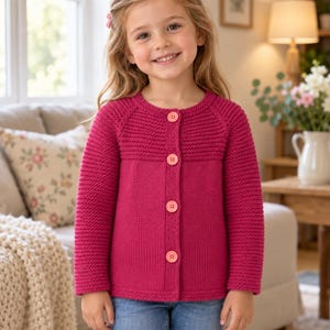 May include: A long-sleeved, fuchsia-colored knit cardigan featuring a round neckline, a textured ribbed yoke, and four light pink buttons down the front. The garment is constructed with a consistent knit pattern on the sleeves and body.