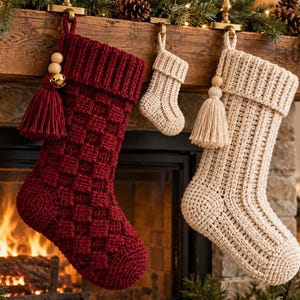 May include: A large deep red crochet stocking with a basketweave pattern, a smaller cream crochet stocking, and a tiny cream crochet stocking. The large stockings feature a folded cuff, a wooden bead, and a matching yarn tassel with a gold bell.
