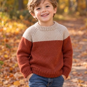 Peut inclure: Un pull en tricot à manches longues présentant un design color-block avec une partie supérieure beige et une partie inférieure orange rouille, associé à un jean bleu. Le pull possède un col rond, des poignets et un ourlet côtelés.