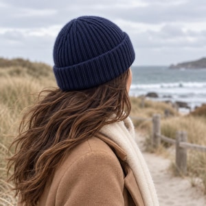 May include: A dark navy blue ribbed knit beanie hat with a folded cuff. The hat features a vertical textured pattern and is constructed from a soft knit material, providing a snug fit around the crown of the head.