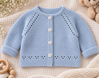 May include: A light blue long-sleeve knit cardigan featuring a round neckline, four white flower-shaped buttons down the centre, and decorative eyelet detailing along the raglan sleeves and the bottom hem of the garment.