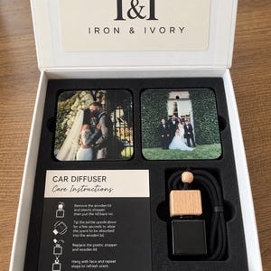 May include: A white gift box labeled I&I Iron & Ivory containing two square photo ornaments, a black car diffuser bottle with a wooden lid and black cord, and a card with Car Diffuser Care Instructions printed in black and white text.