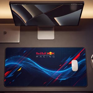 May include: A rectangular desk mat featuring the Red Bull Racing logo in the center. The design includes a dark blue background with abstract blue light waves, red and yellow geometric accents, and a white computer mouse on the right side.