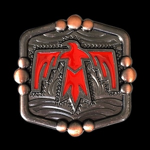 Może przedstawiać: Srebrna klamra do paska z czerwonym, stylizowanym wzorem ptaka indiańskiego.