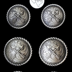 以下が含まれることがあります： ロープのような縁取りのある、銀色の丸いコンチョが6つ。各コンチョは、交差した矢印と花の模様が特徴です。背景は黒で、右上に「HA）」とテキサスの白いアウトラインがあります。