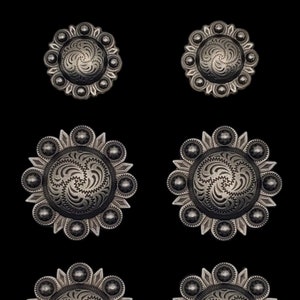 May include: Six silver-toned metal conchos with a decorative swirl design. The conchos have a raised edge and are surrounded by a ring of small beads.