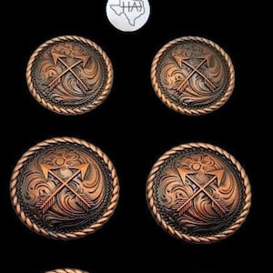 以下が含まれることがあります： ロープ状の縁取りと、中央に太陽の光が差し込む2本の交差した矢印のデザインが施された、銅色の金属製のボタンが6つあります。