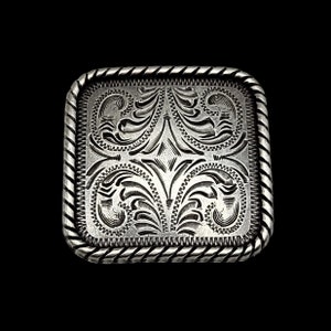 May include: Silver belt buckle with a square shape and a rope-like border. The buckle features an intricate, engraved floral design.