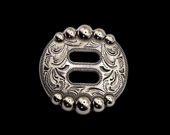 May include: Silver-toned metal buckle with a decorative engraved design and a double-loop opening. The buckle is surrounded by a row of small, round beads.