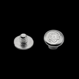 Peut inclure: Deux rivets métalliques argentés. L'un a une tige filetée et une base plate. L'autre a une tête bombée avec un motif floral. Idéal pour la maroquinerie.