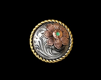 May include: A silver and gold concho with a copper flower design and a green stone in the center. The concho has a rope-like border.