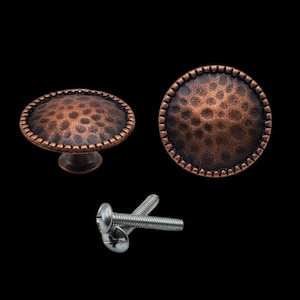 May include: Two copper-toned cabinet knobs with a hammered finish and a decorative border. The knobs are shown with two silver screws.