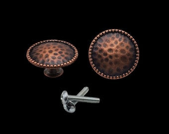 Puede incluir: Dos pomos de armario de color cobre con acabado martillado y borde decorativo. Los pomos se muestran con dos tornillos plateados.