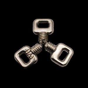 Puede incluir: Tres ganchos de metal plateado con bucles cuadrados y extremos roscados. Los ganchos están dispuestos en forma triangular.