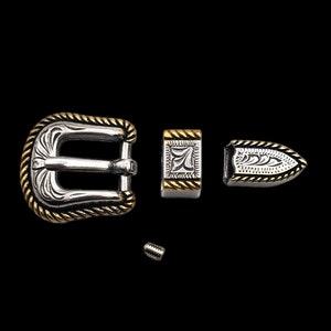 Pode incluir: Uma fivela de cinto prateada com um design de corda dourada ao redor da borda. A fivela tem um design gravado decorativo. A fivela vem com uma ponta e um prendedor correspondentes.