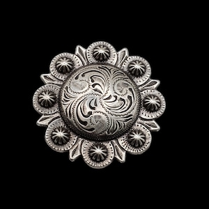 May include: A silver-toned metal concho with a floral design. The concho has a circular shape with a raised center and a scalloped edge.