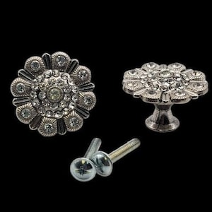 May include: Two silver drawer pulls with a flower design and rhinestones. The pulls come with two screws.